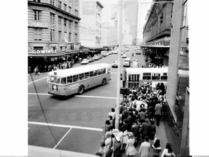 Pedestrians and buses with Alan Davis advertising in ci...