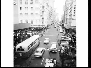 Pedestrians and buses with Alan Davis advertising in ci...