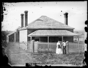 Couple in front of brick house with shingle roof, three...