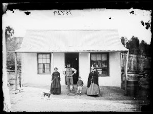 Man, two women and a boy outside a whitewashed house wi...
