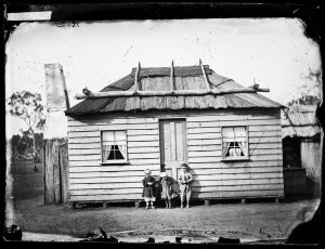 Children outside weatherboard house with bark roof, Gul...
