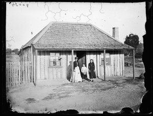 Woman and children in front of slab house with shingle ...