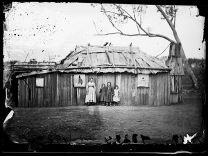 Mother and girls outside slab hut with bark roof, Gulgo...