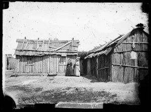 Two women with slab and bark houses