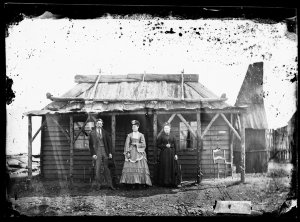 Man and two women with bark roof, weatherboard house, G...