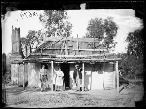 2 men and a woman with bark-roofed, whitewashed house, ...
