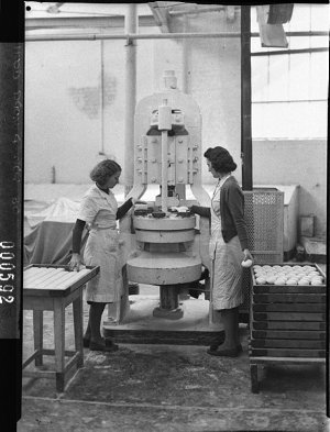 Two women operating a rubber moulding machine making ca...