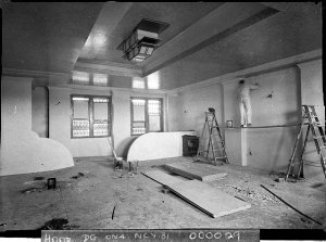 Workmen plastering the walls of the dress circle foyer,...