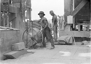 Workmen mixing and pouring concrete with small hand-whe...