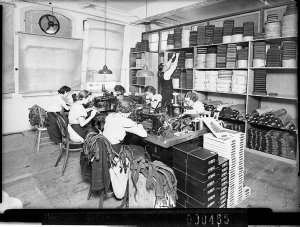Women in the foreground machining as storeman stacks th...