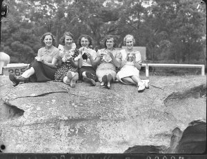 Five young women sitting on a rock, eating their ice-cr...