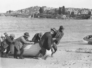 Men pulling fishing boat up Coogee Beach; steel towers ...