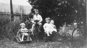 Children sitting on toys in garden - Temora, NSW