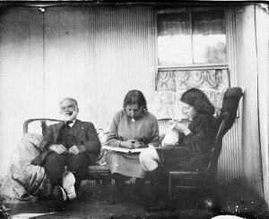 Relaxing on the verandah. Man smoking, girls reading an...