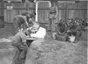 Army cooks tending the 'Dixies' over the camp oven; sol...