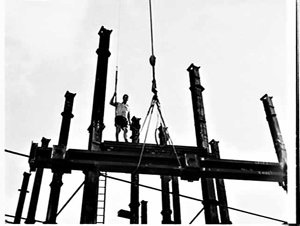 Building labourer on girders being hoisted by crane to ...