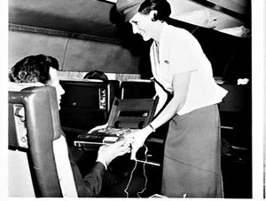 Alitalia flight attendant helps a passenger with a tape...