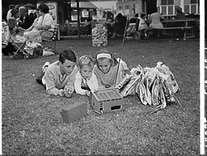 Children with showbags lying on the grass watching a po...