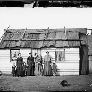 Women and children in front of a weatherboard house wit...
