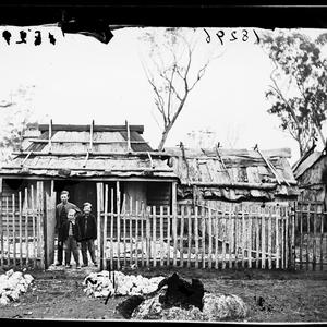 Children outside weatherboard house with bark roof and ...