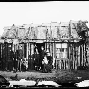 Family outside slab hut with bark roof, Gulgong