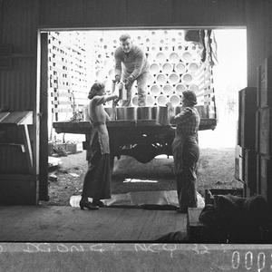 Two women and a man stacking cans of paint on a truck