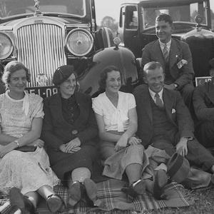 A group watching the game from the sidelines.  Cars are...