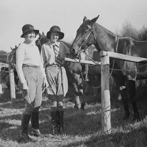 Two young woman with riding gear with their horses