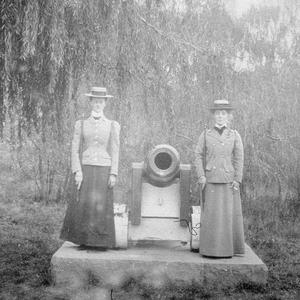 Two women standing next to a cannon (in a soldierly sta...