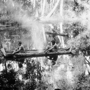 Two Aboriginal men in canoe, with fire in canoe, in a s...