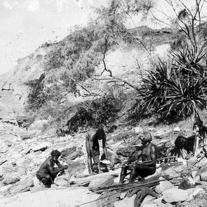 Three Aboriginal men on beach making tools & weapons - ...