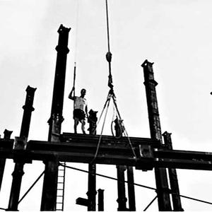 Building labourer on girders being hoisted by crane to ...