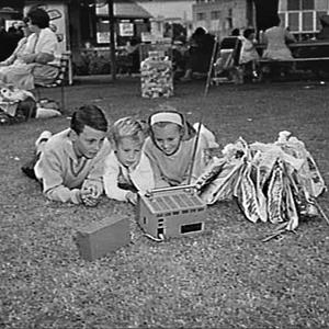 Children with showbags lying on the grass watching a po...